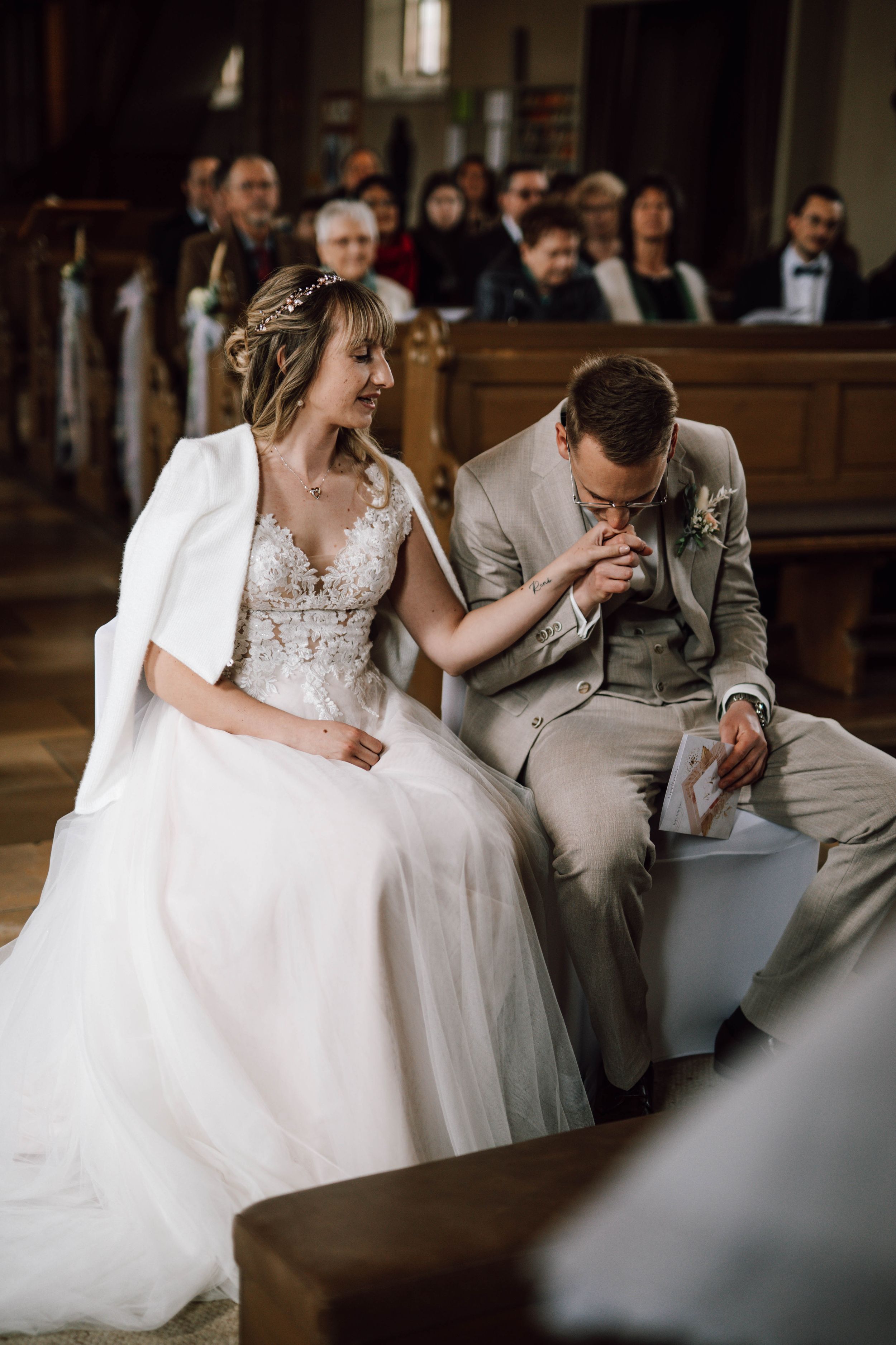 Couple sharing tender moment while seated in church pew during ceremony.