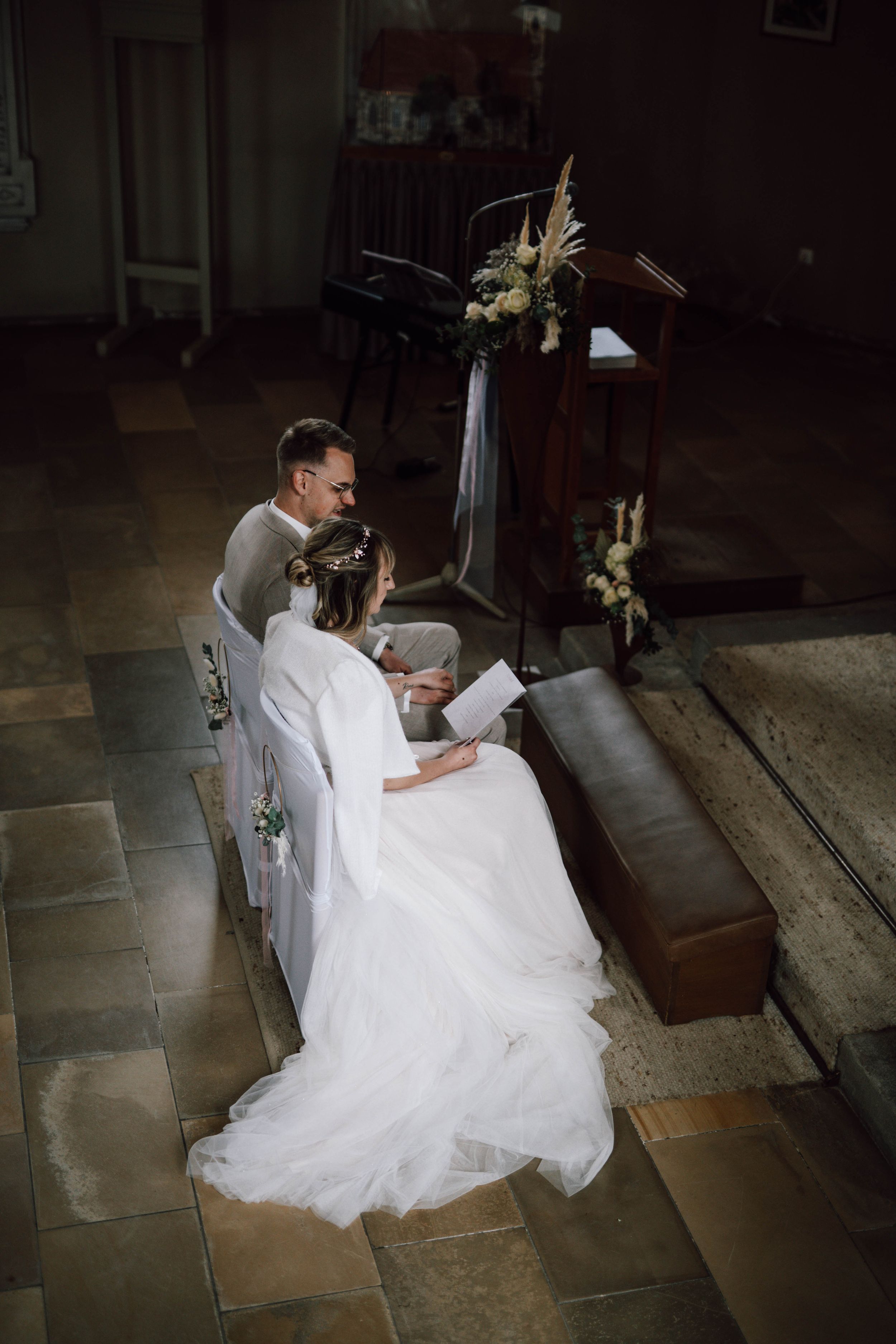 Couple reading letters to each other in dimly lit church setting.