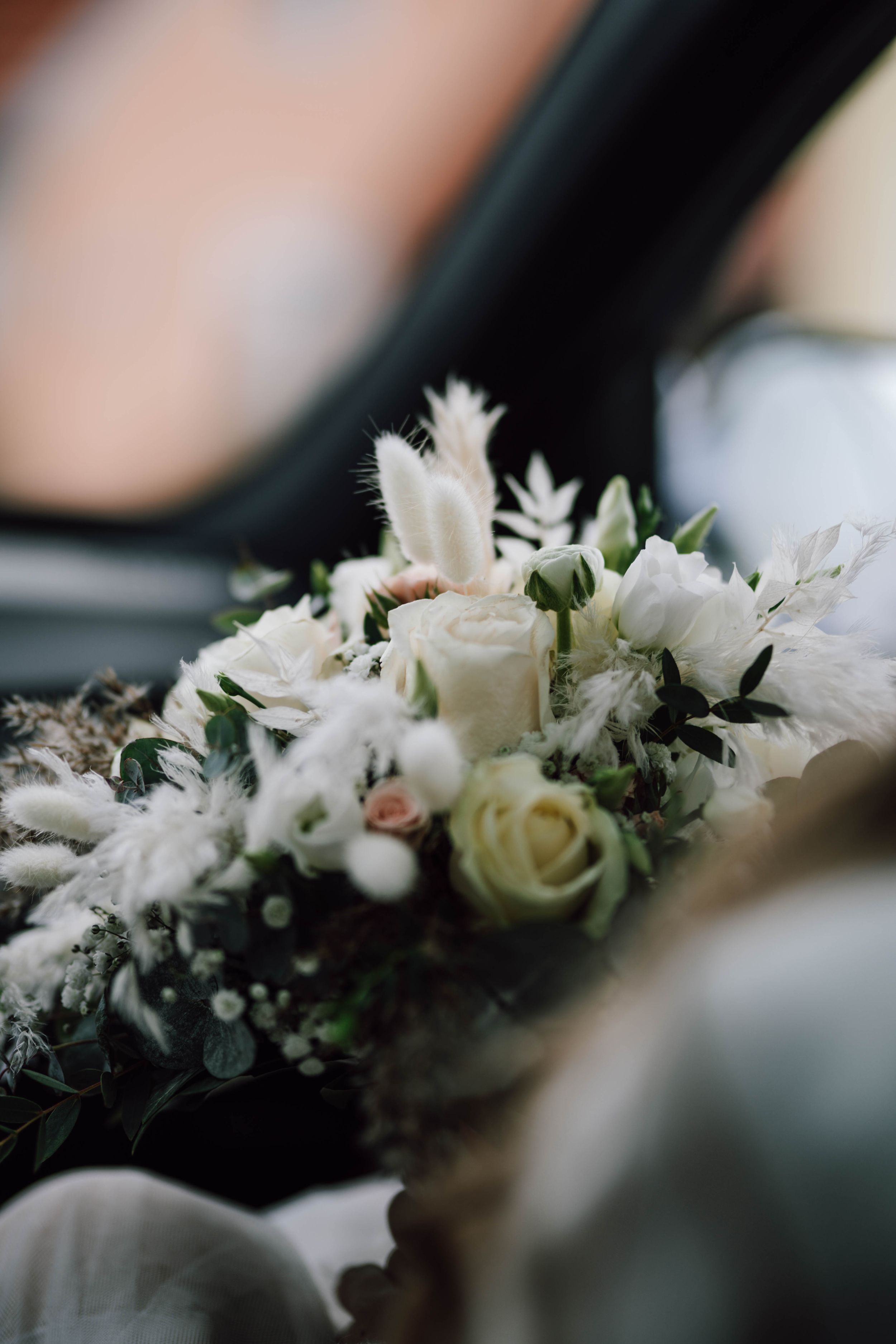 Delicate white wedding bouquet with roses and greenery in soft focus.