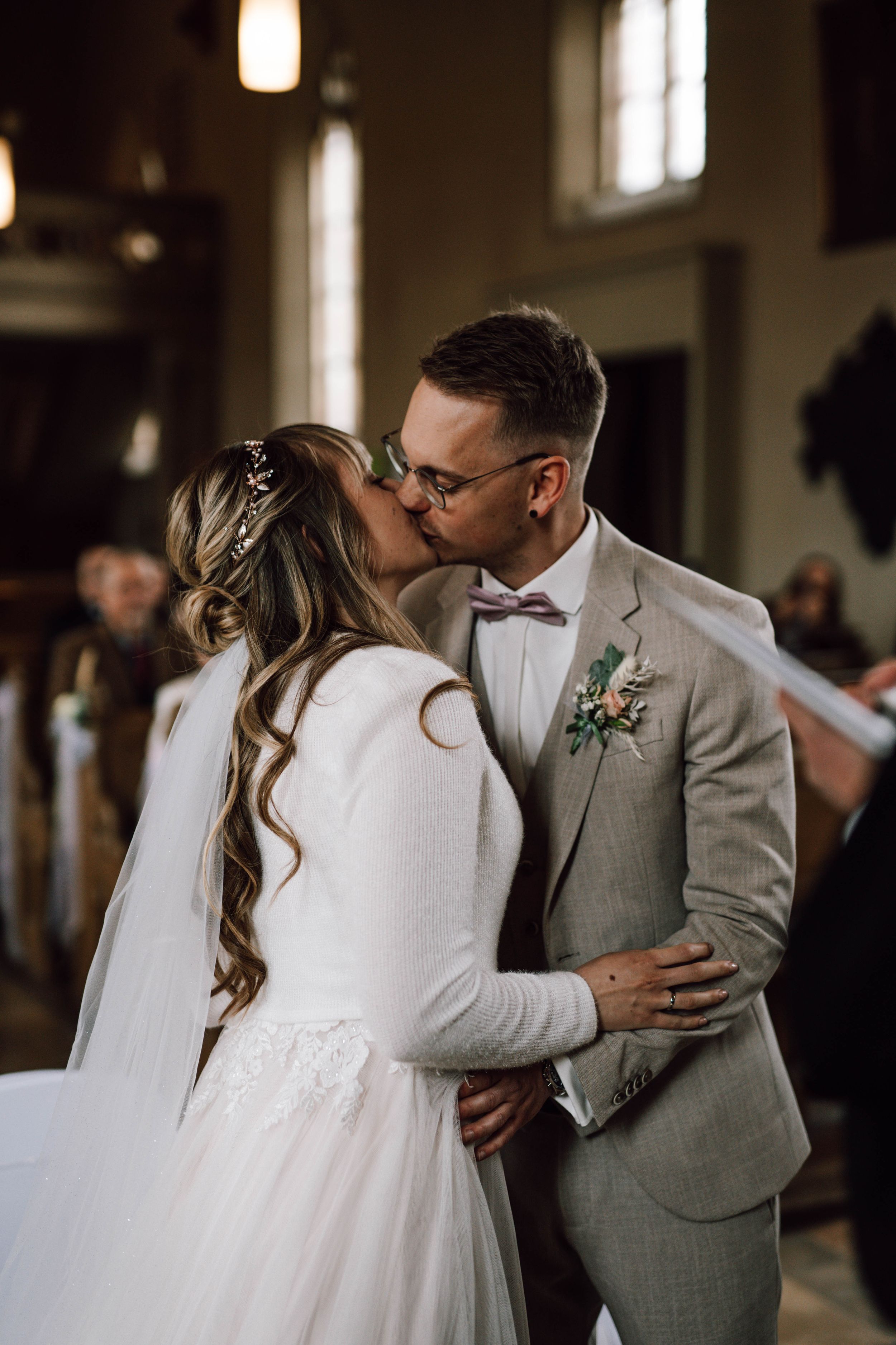 Romantic wedding ceremony kiss between couple in a church with ambient lighting.
