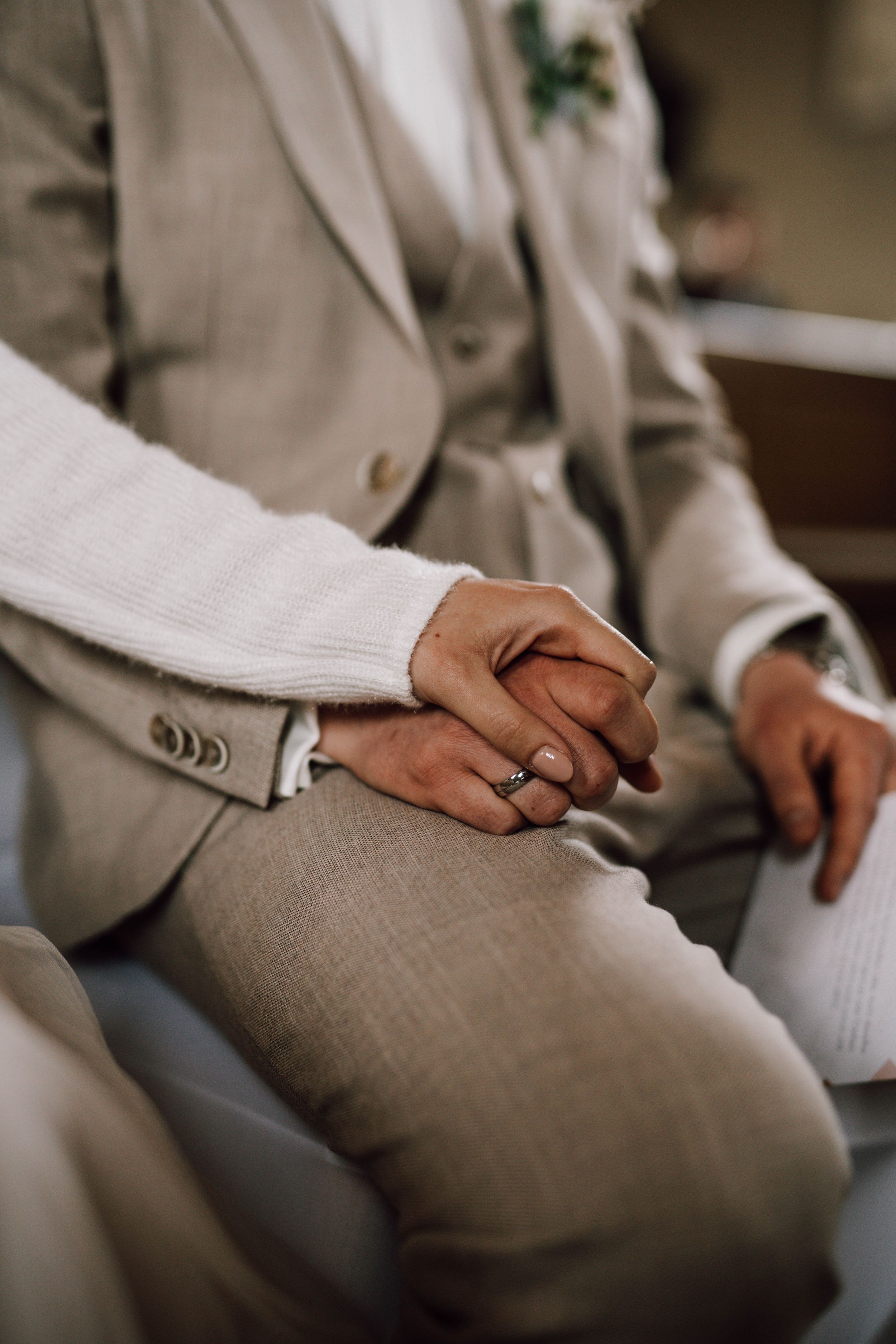 Close-up of clasped hands showing wedding ring against light gray suit.
