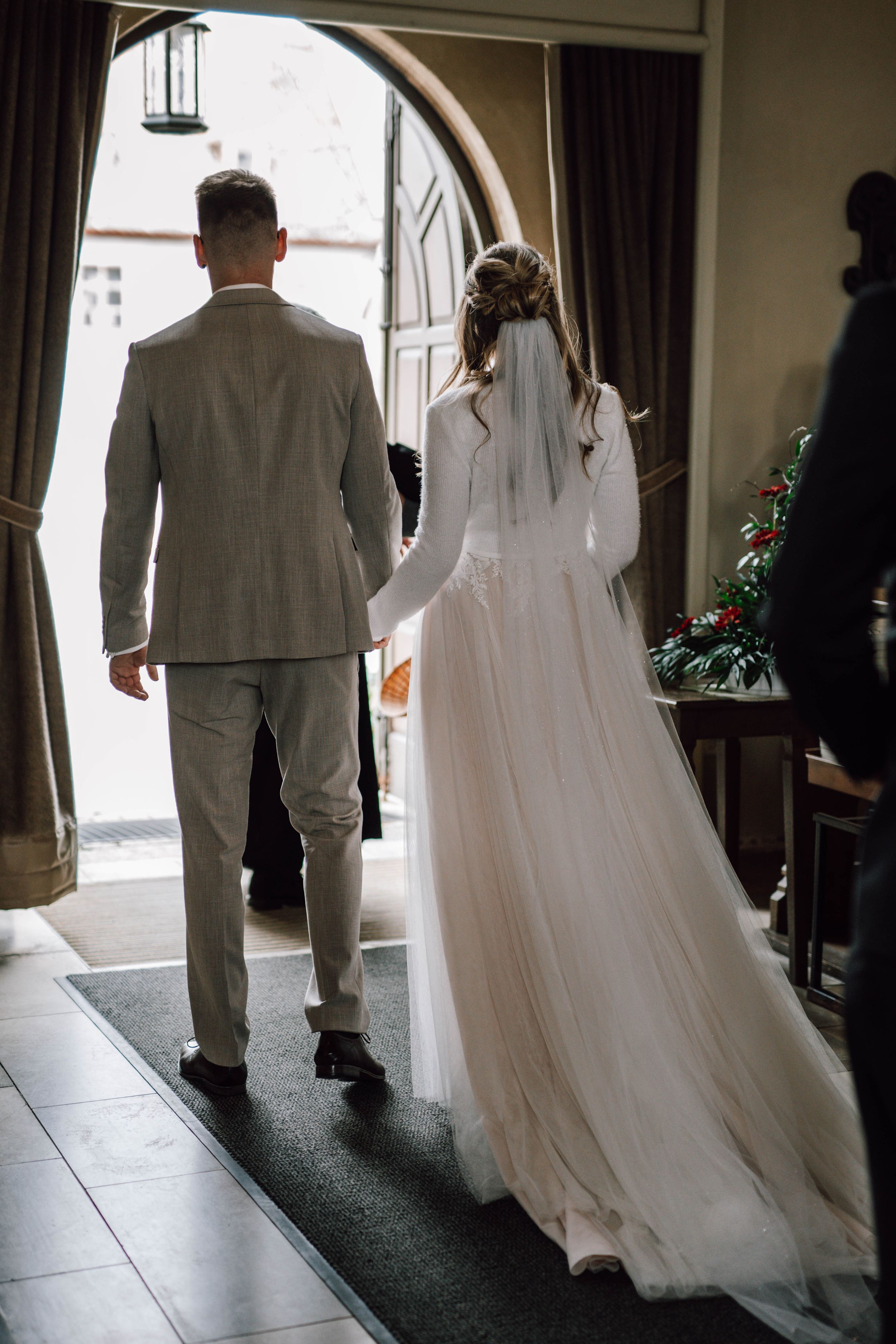 Newlyweds walking through arched doorway after ceremony in elegant attire.