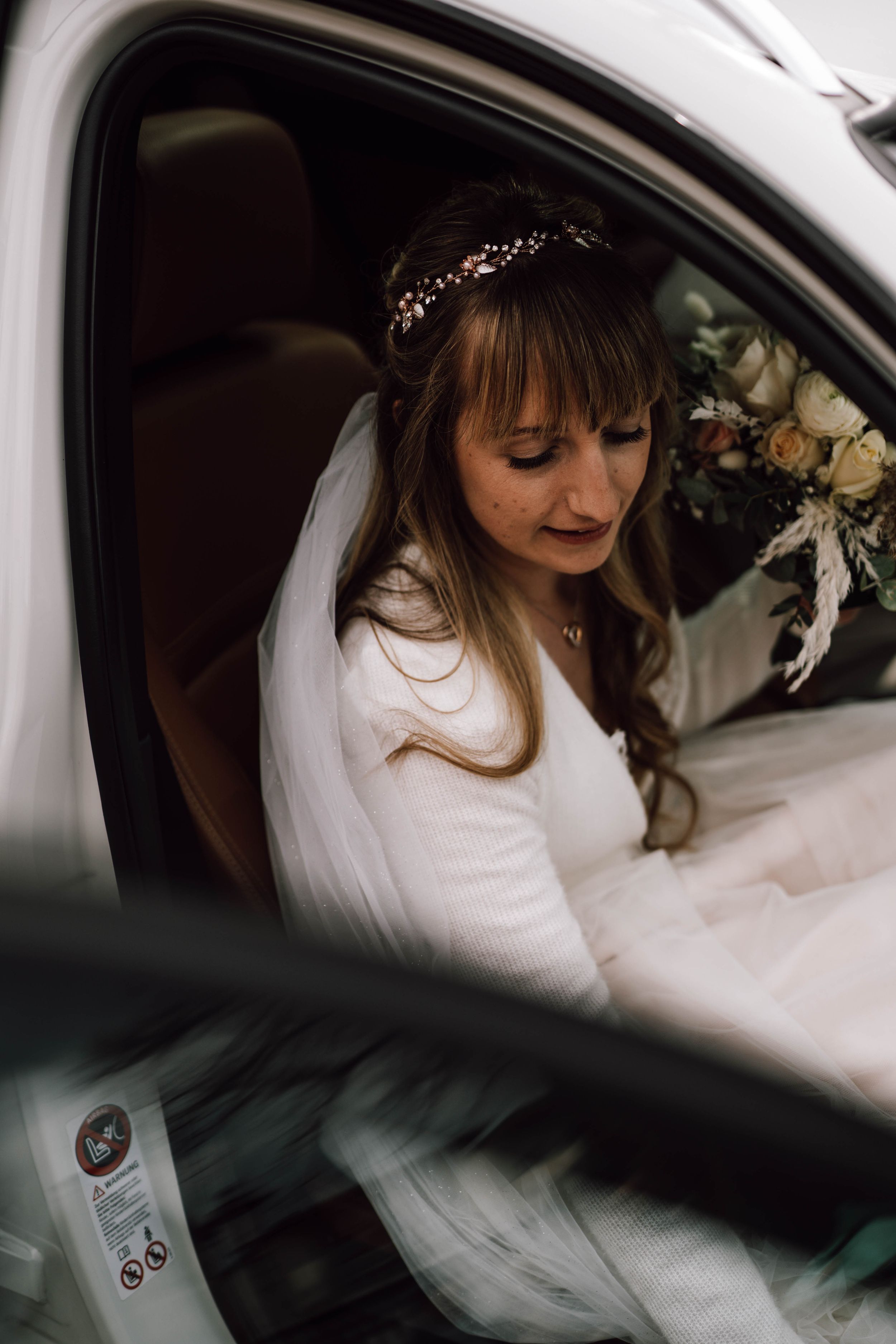 Bride in white dress and crystal headpiece sitting in car before ceremony.