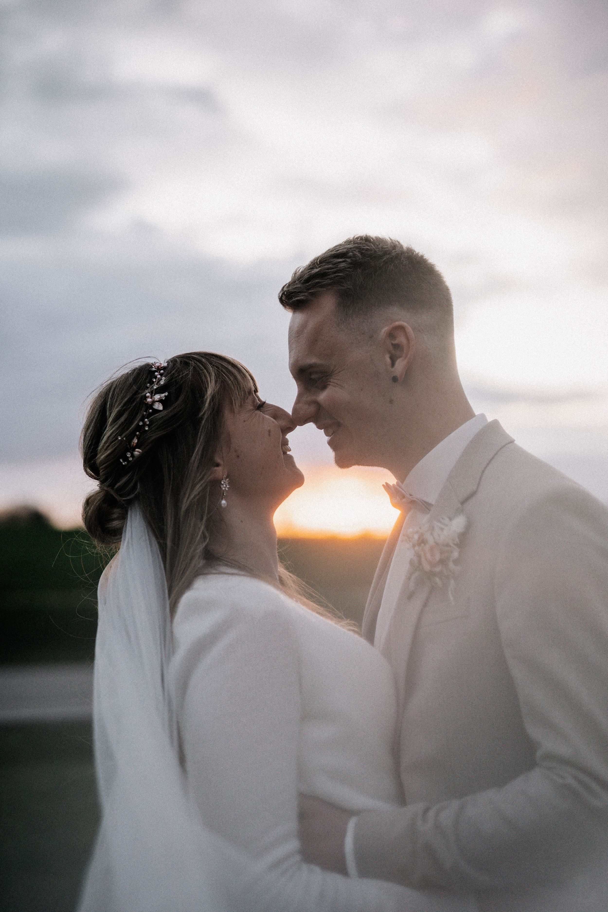 Romantic sunset portrait of newlyweds in white and beige attire.