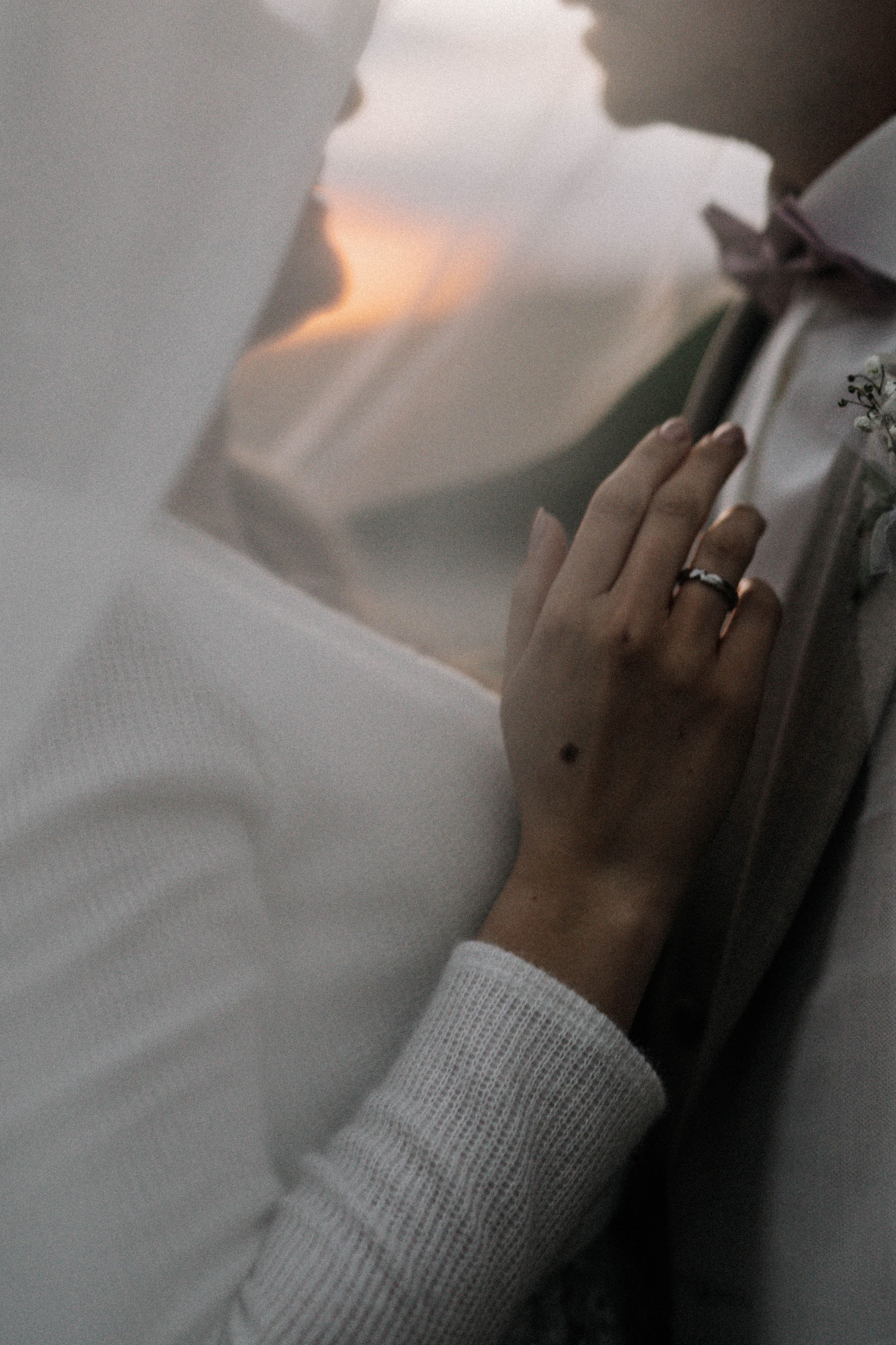 Close-up shot of hands resting on soft white bedding in moody lighting.