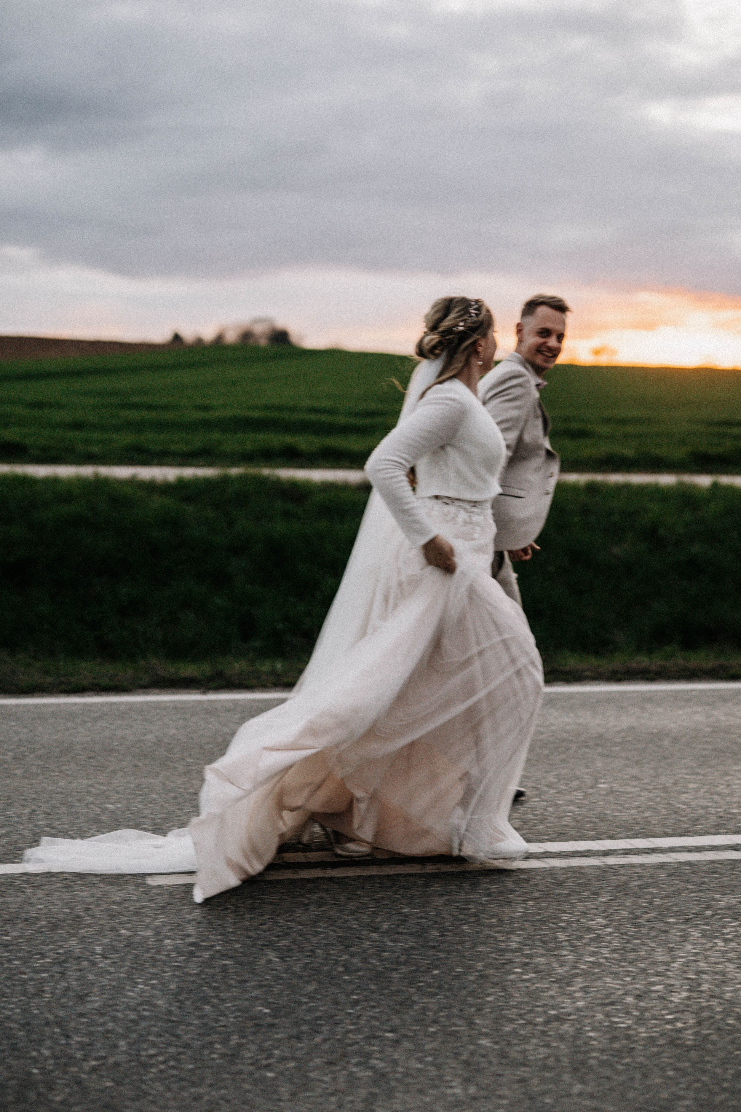 Wedding couple dancing on a road at sunset with flowing white dress.