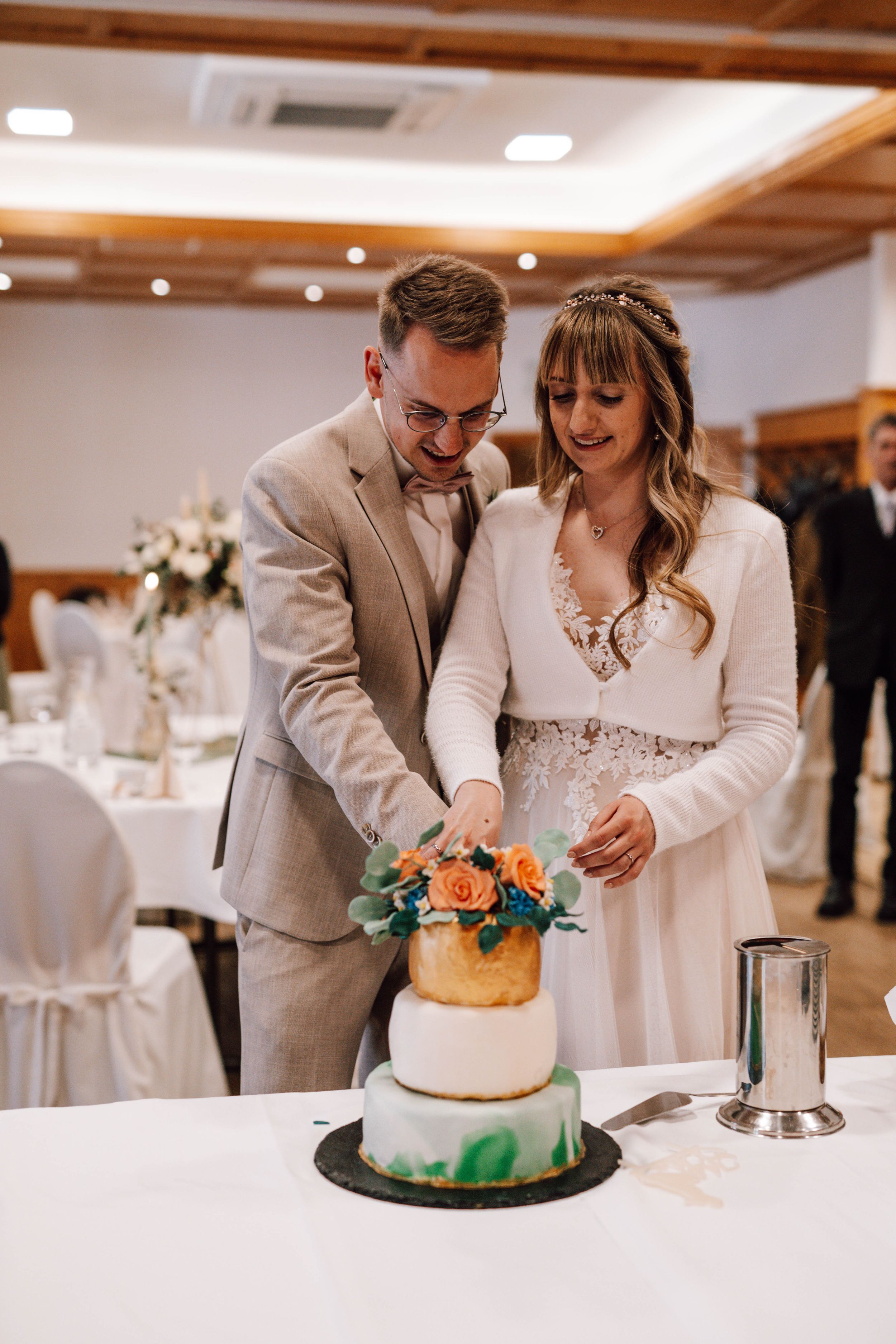 Wedding couple cutting their orange and white tiered cake together at reception.