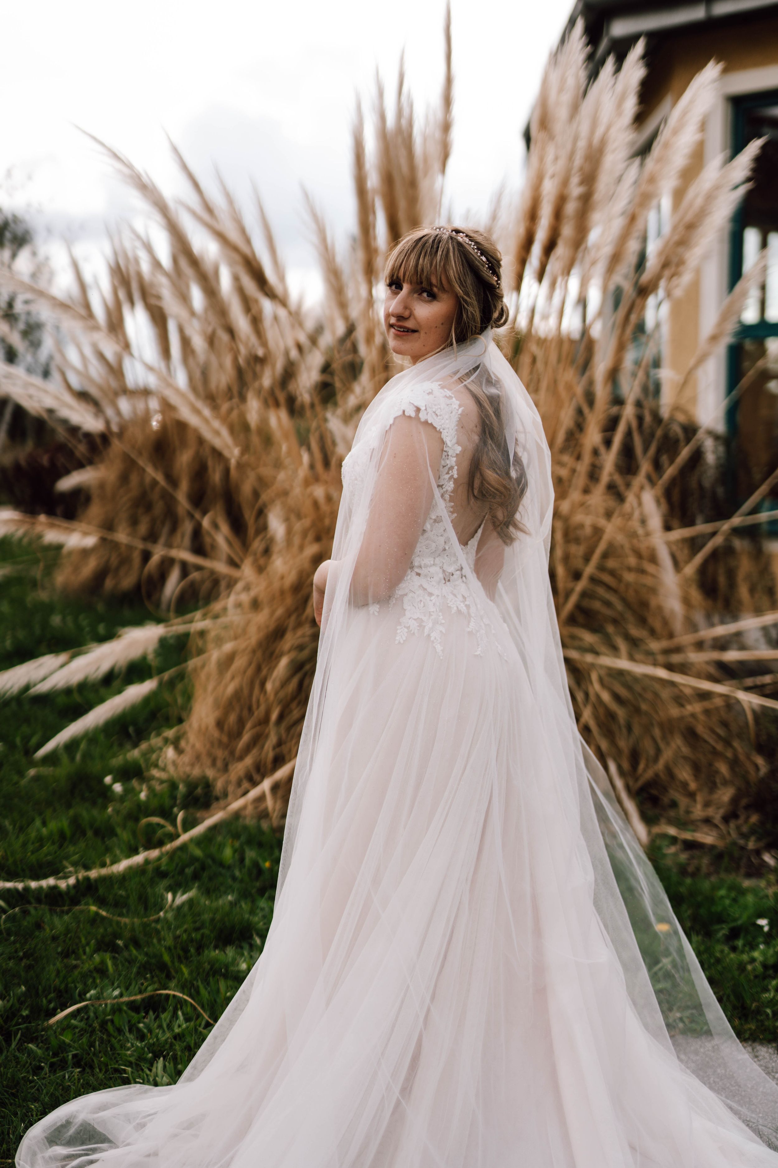 Flowing white wedding dress with lace details photographed against dried pampas grass.