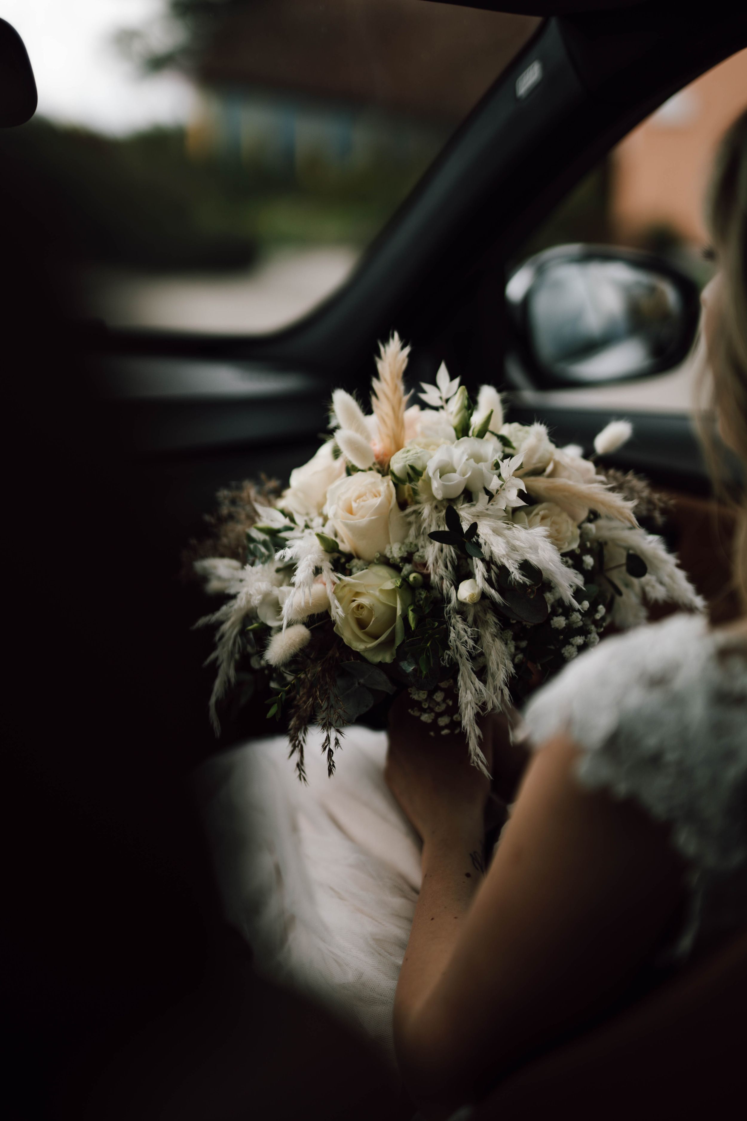 Delicate white and cream floral bouquet with feathers in car interior.