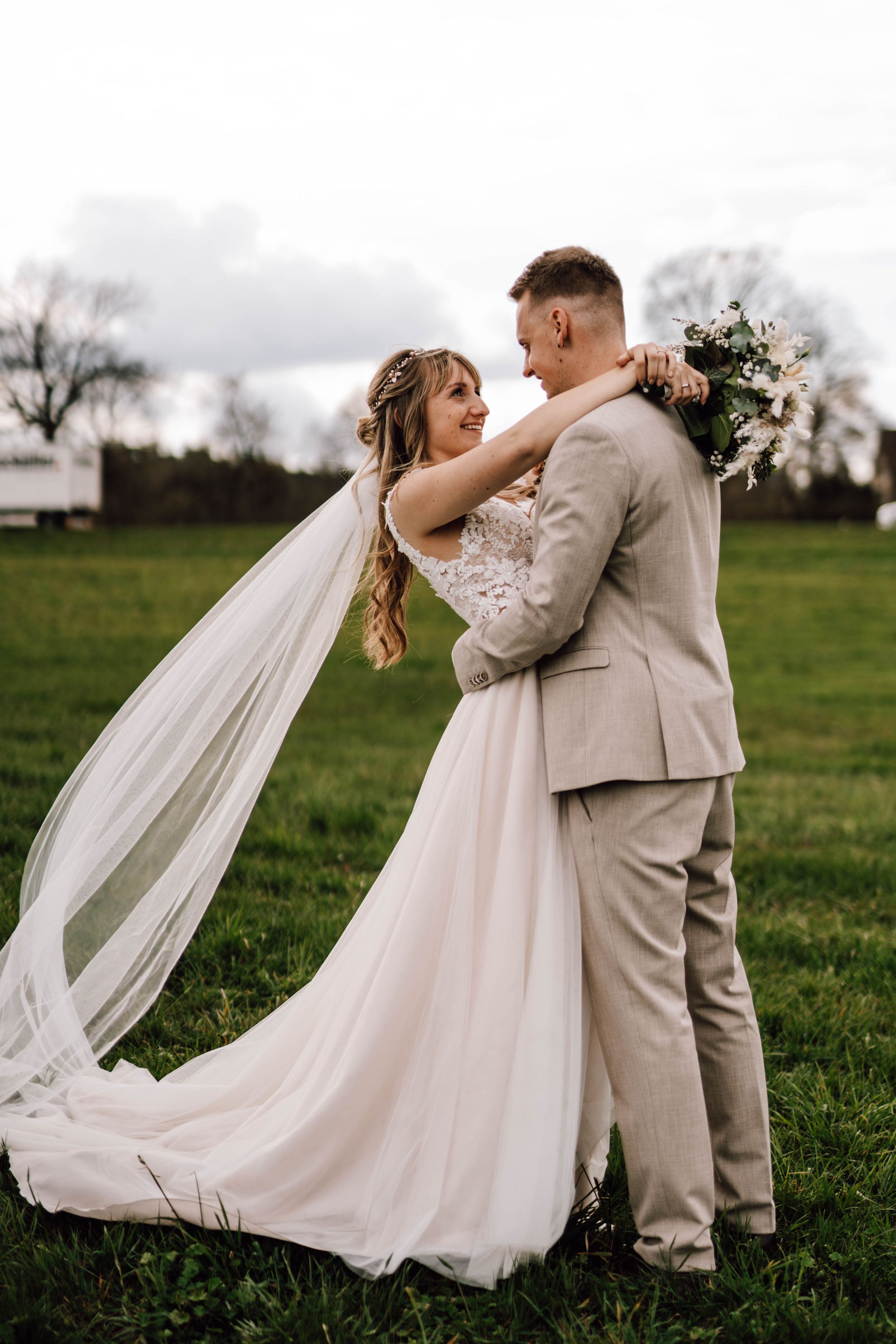 Romantic wedding couple embracing in green field with flowing veil.