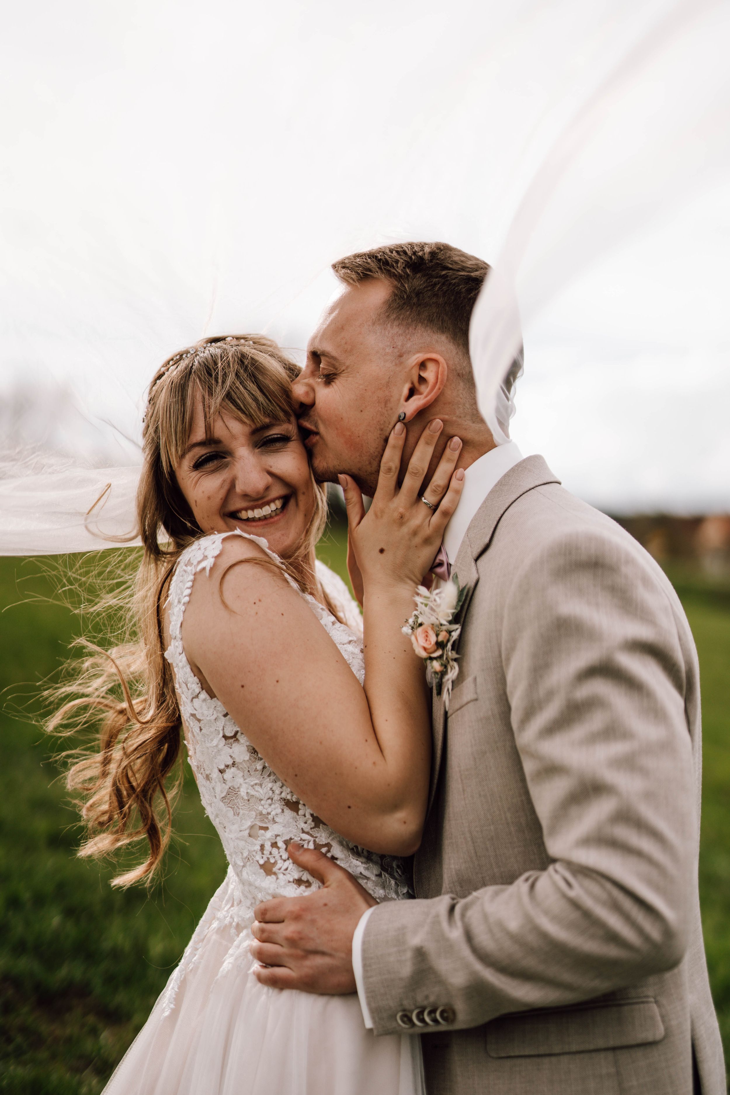 A joyful wedding moment captured in a green field with the couple sharing an intimate embrace.
