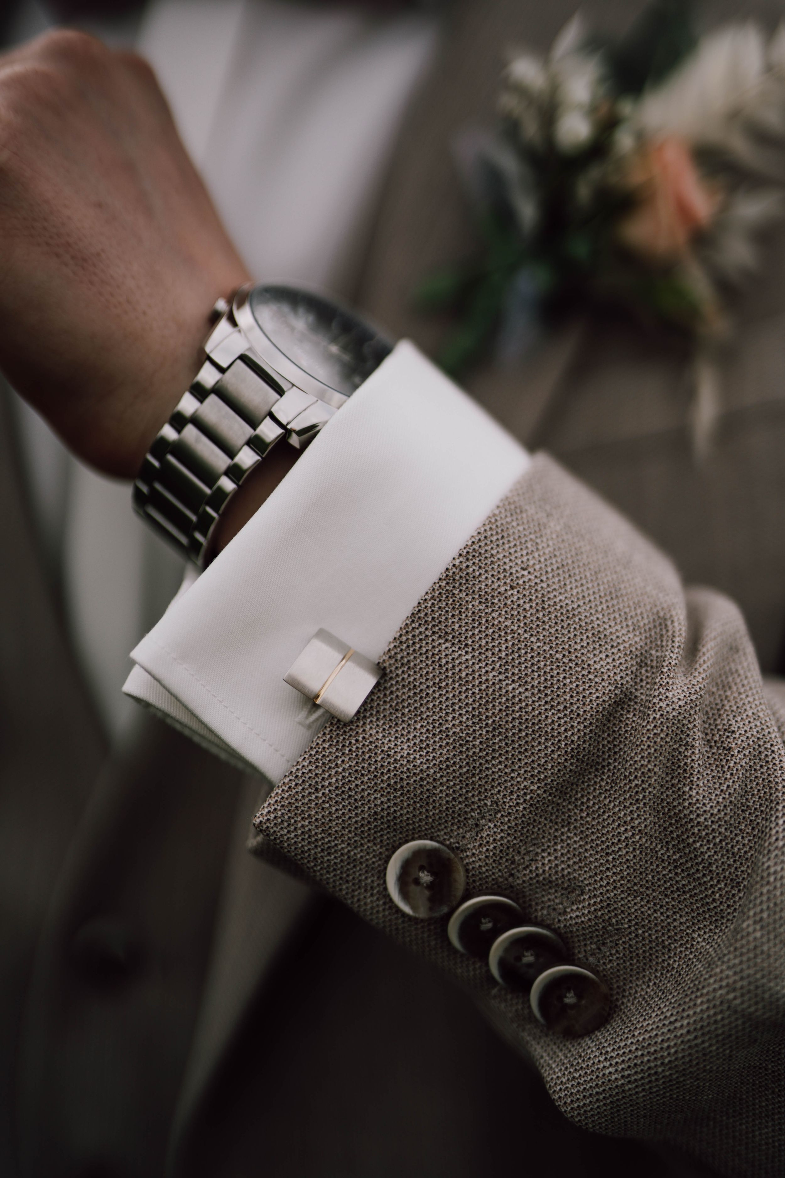 Close-up of groom's sleeve showing silver watch and white cufflink detail.