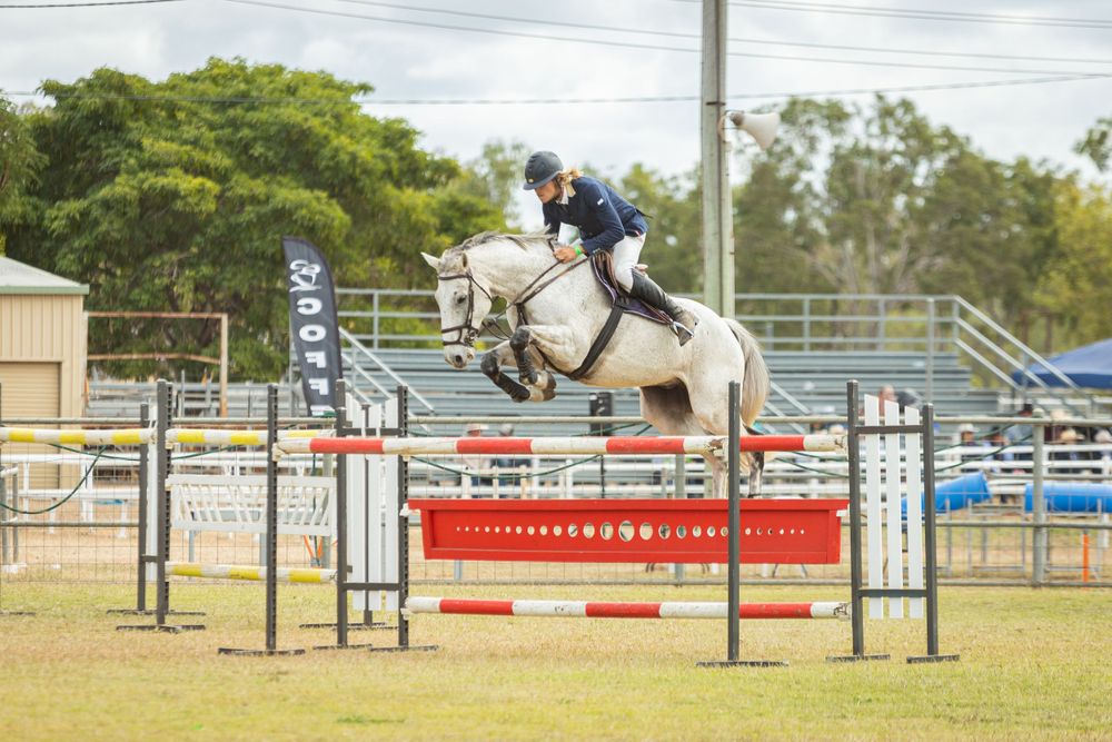 Horse and rider clearing a red and white jump fence during an equestrian event.
