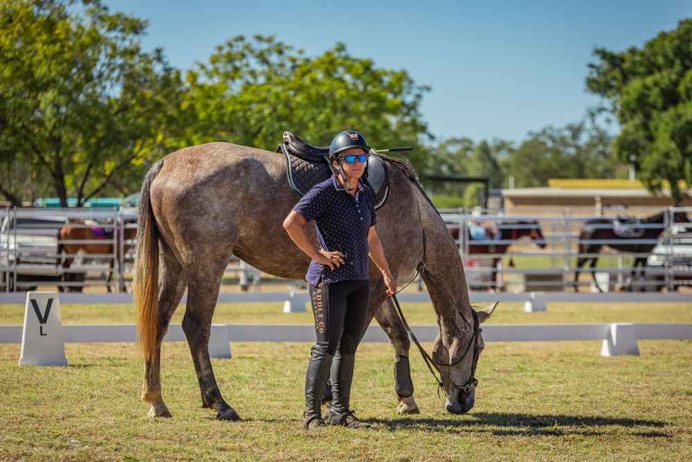 Horse grazing peacefully in competition grounds while being monitored.