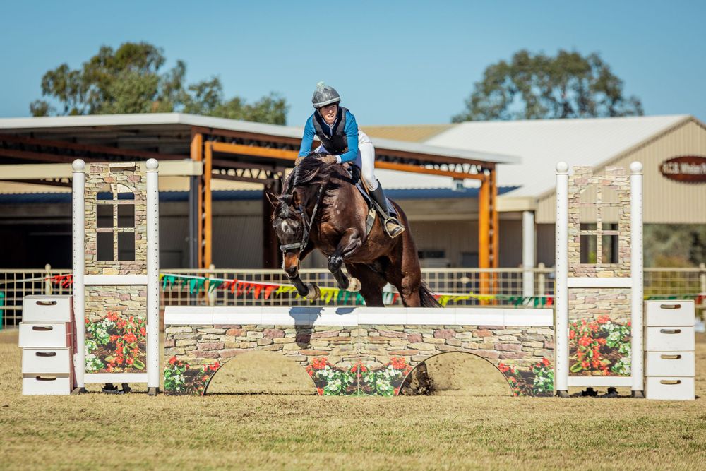 Horse and rider in blue clearing a decorated show jumping fence during competition.
