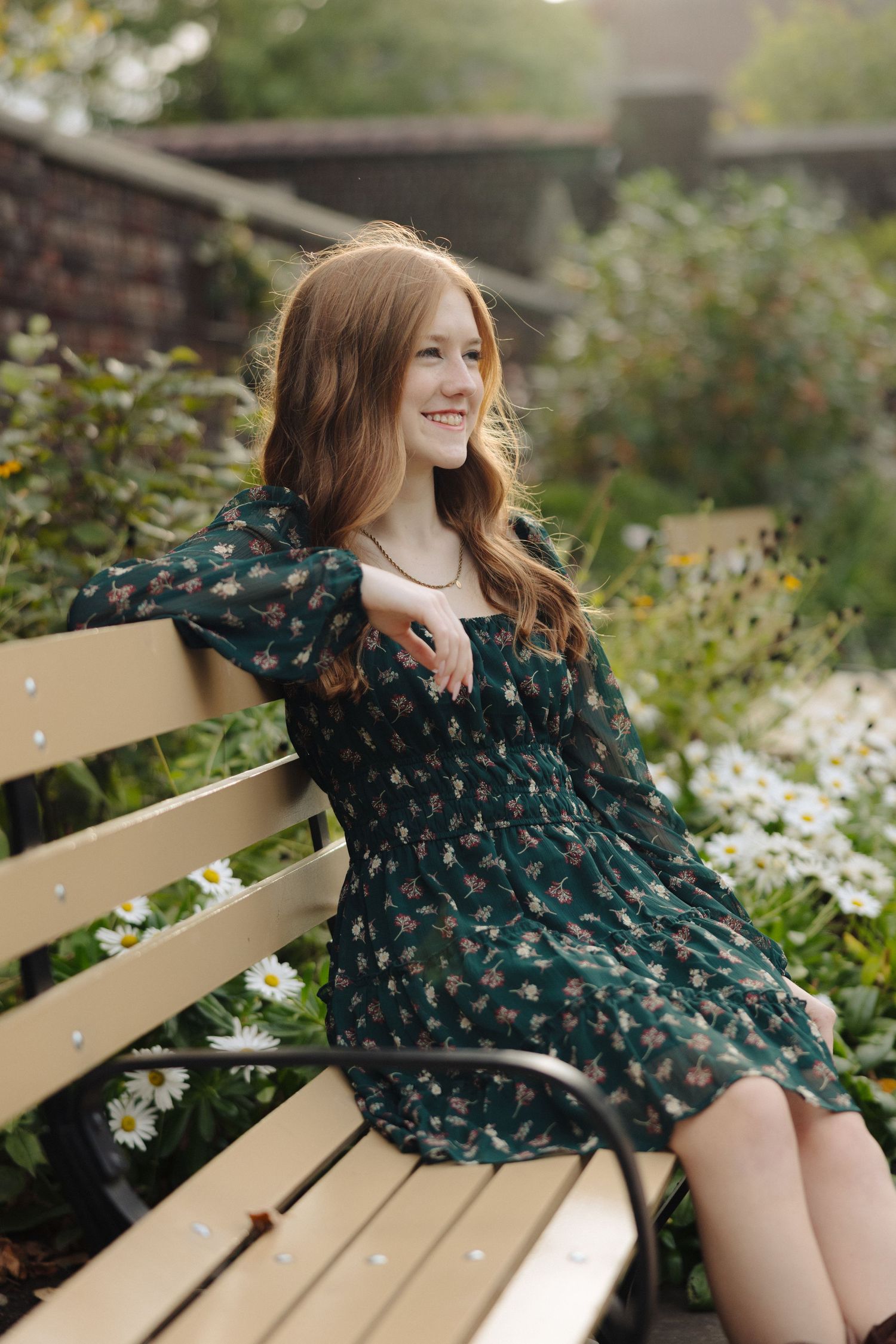 Portrait of a woman in a navy floral dress sitting casually on a park bench.