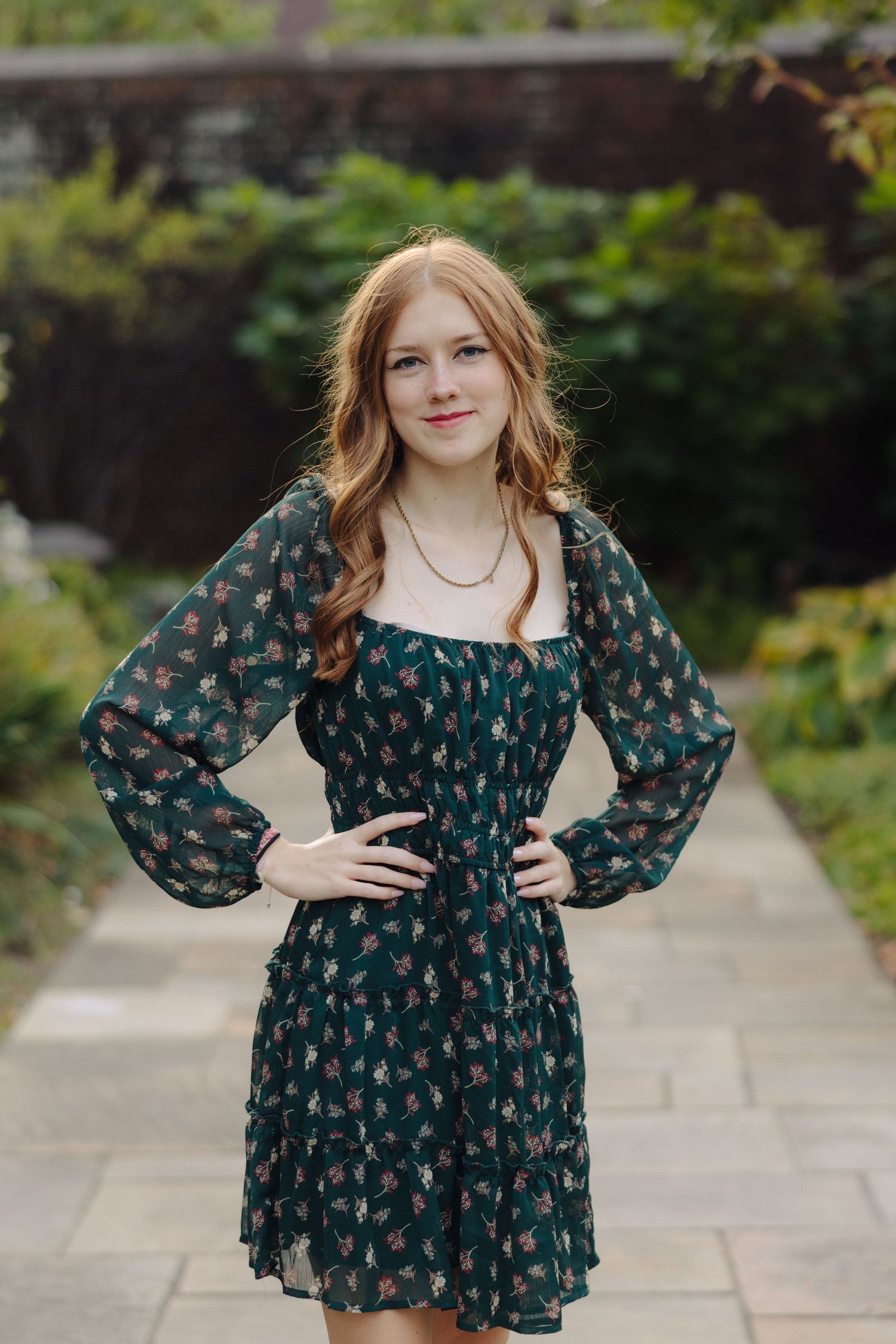 Portrait of someone wearing a dark floral dress with puff sleeves in a garden setting.