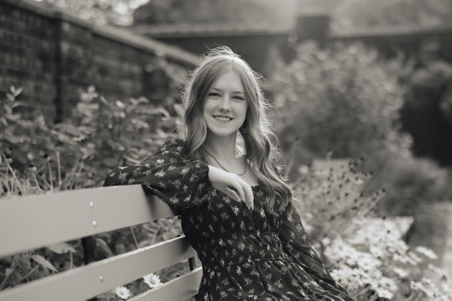 Black and white portrait of a woman in a patterned dress sitting on a garden bench.