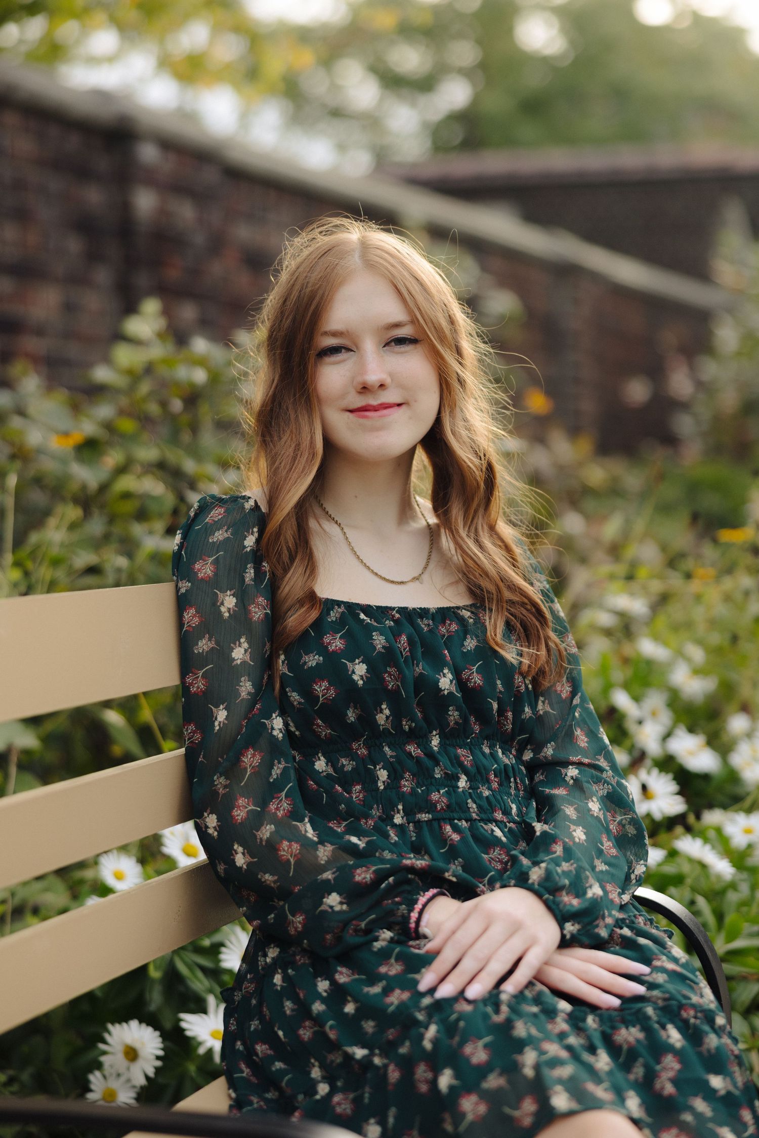 Elegant woman in vintage-style dress poses on bench amidst garden greenery.