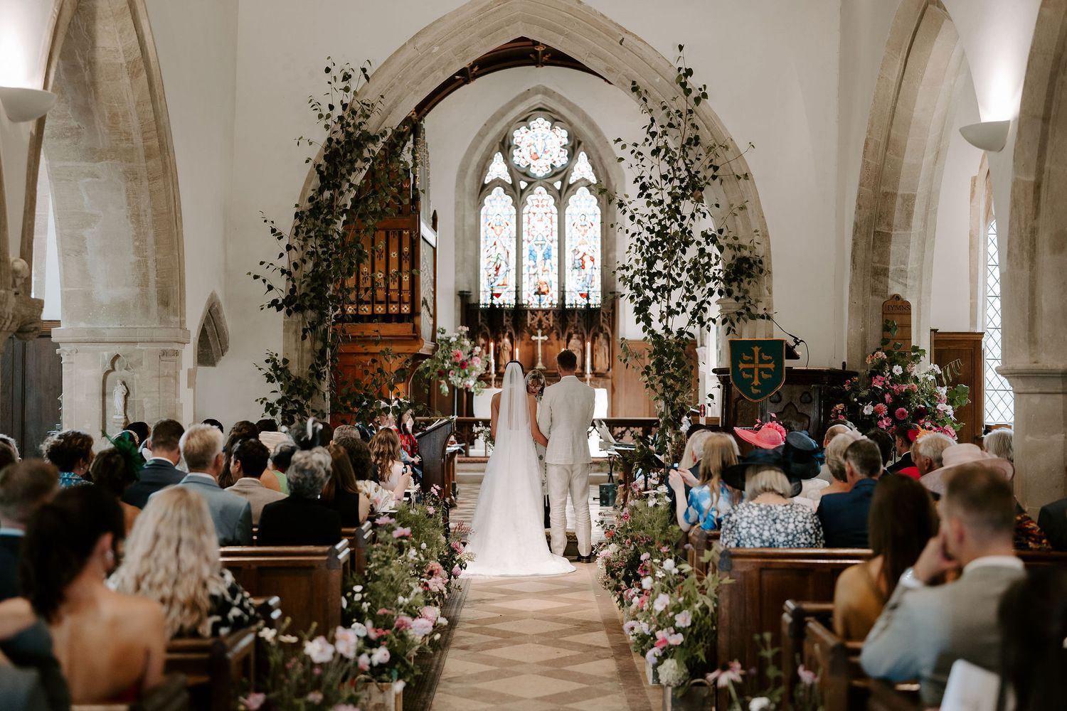 bride and groom stood at the alter surrounded by wedding guests at st Nicholas church in Oxfordshire