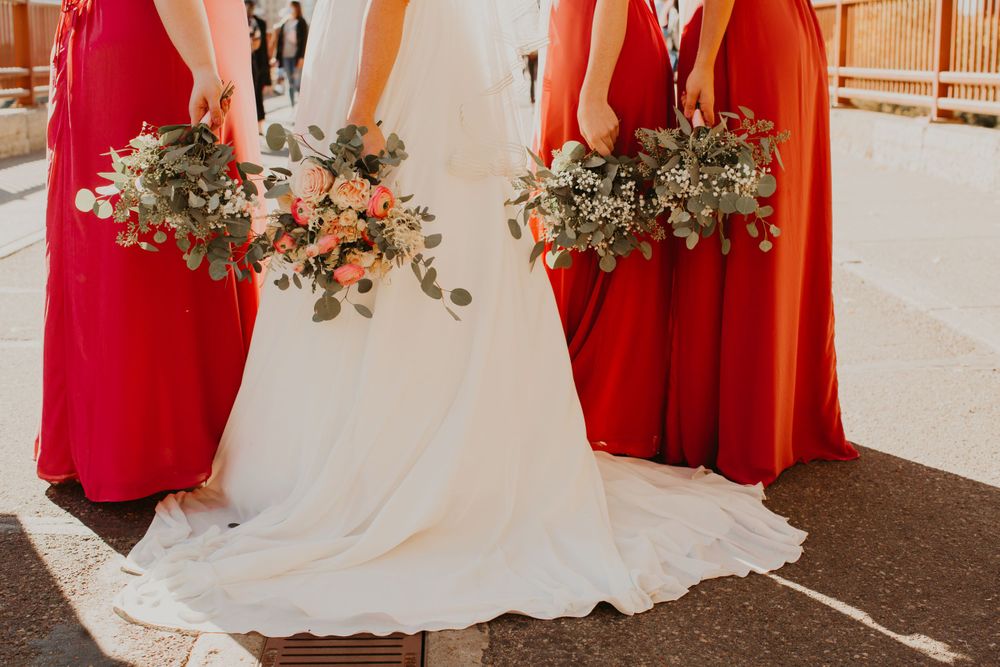 Close-up of bride in white gown and bridesmaids in red dresses holding elegant floral bouquets.