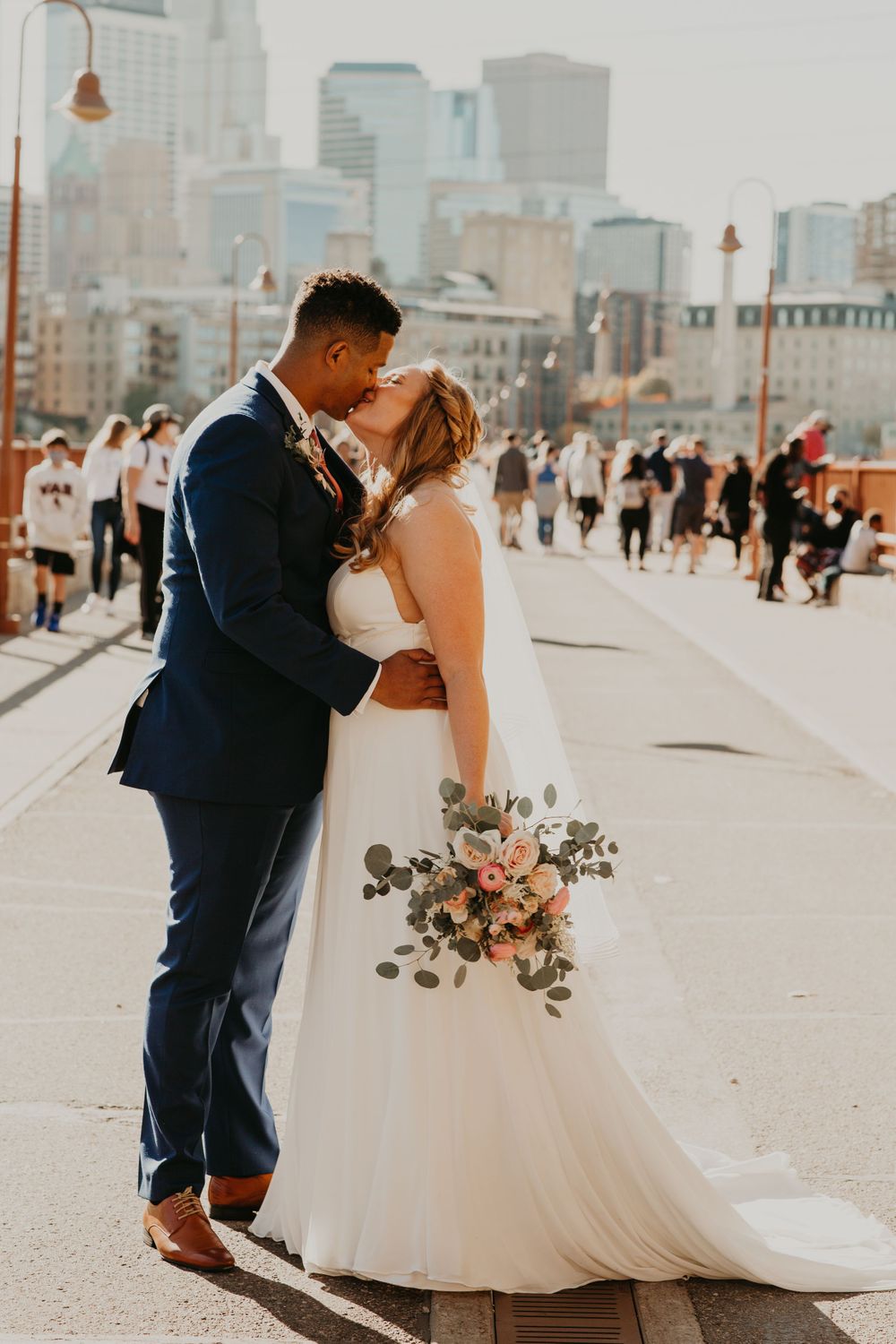Bride and groom share a kiss on a busy urban bridge with city skyline in the background.