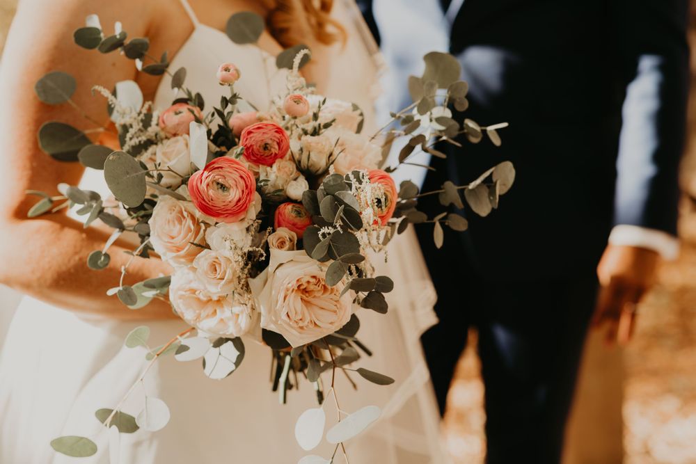Close-up of bridal bouquet with peach roses, coral ranunculus, and eucalyptus greenery.