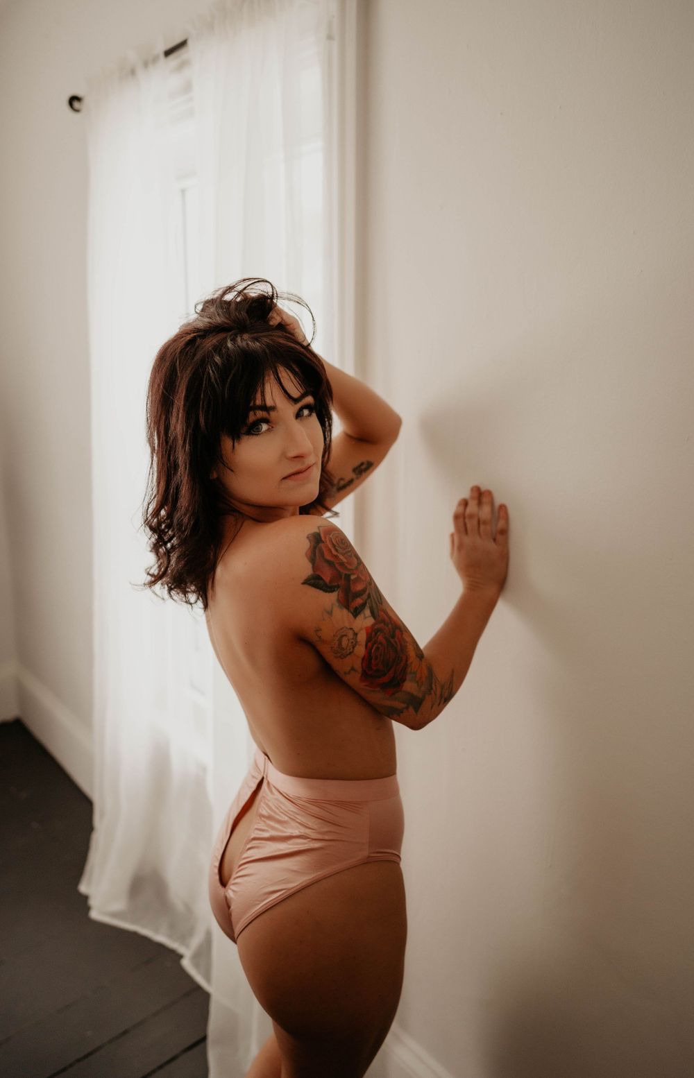 Minimalist portrait against white curtains showcasing tattoo art.