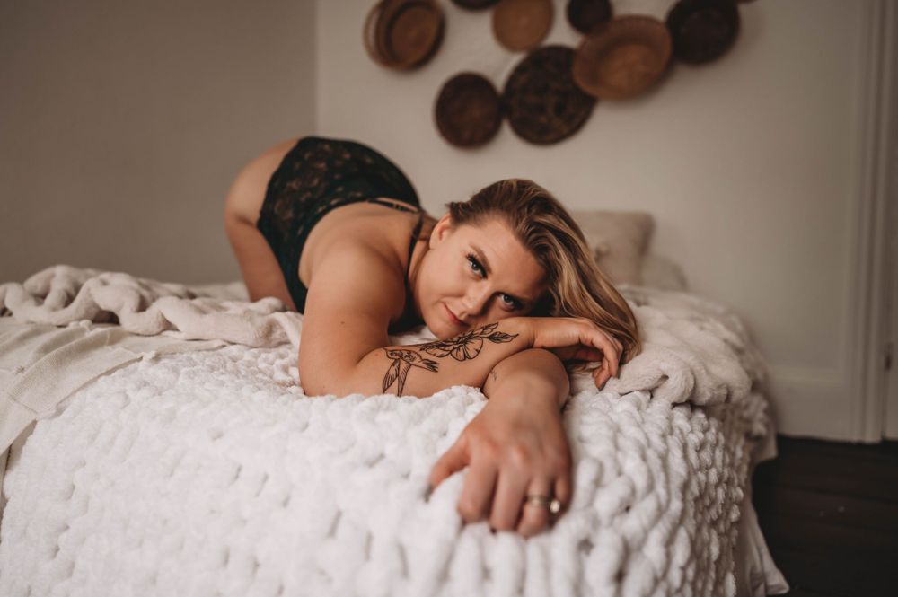 A woman in lingerie lounges on a white textured bedspread in a cozy bedroom setting.