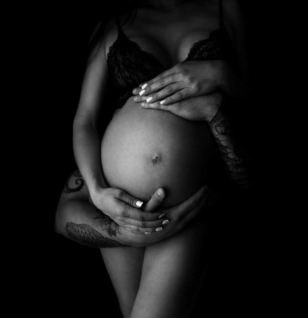 Artistic black and white close-up of hands cradling pregnant belly.