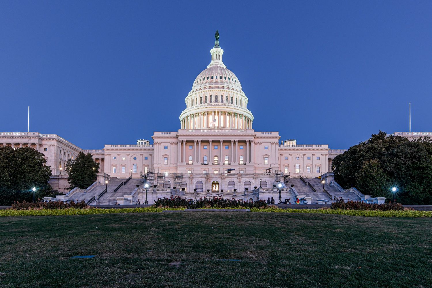 US Capitol building illuminated at dusk with green lawn in foreground.