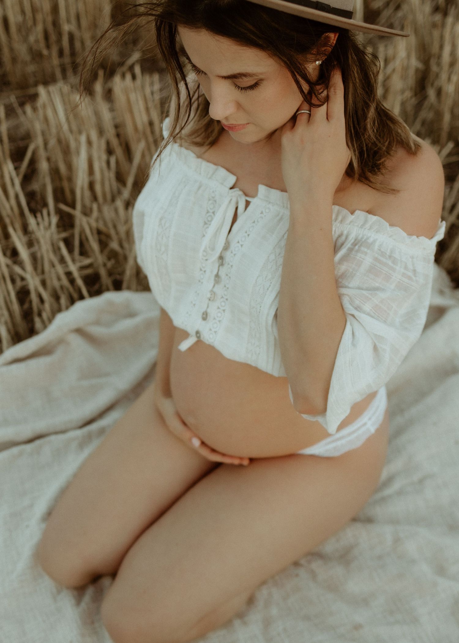 Expecting mum sitting amongst dry grass during a natural sunset pregnancy photography session at Port Willunga, South Australia