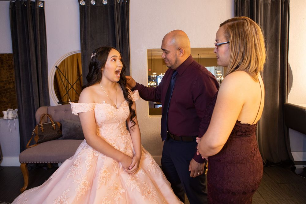 A wedding preparation scene showing stylists helping adjust a pink ballgown dress.