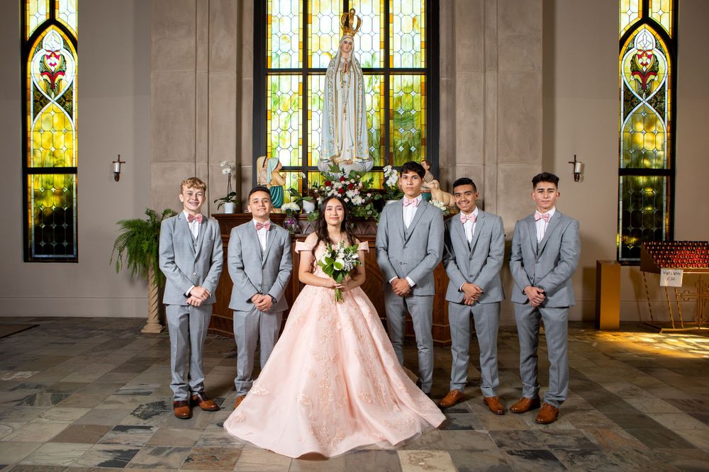 Wedding party in gray suits and pink gown poses in front of stained glass windows.