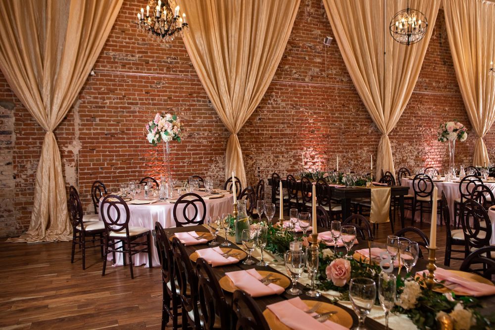 Elegant wedding reception venue with exposed brick walls, draped curtains, and formal table settings.