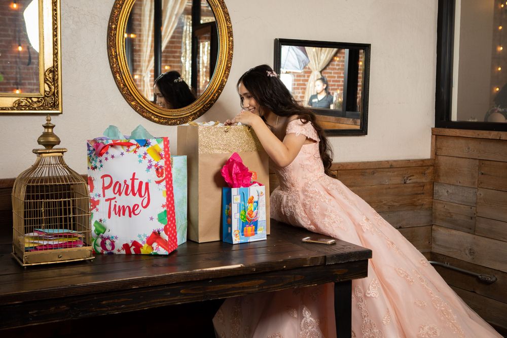 Pink decorative party sign and gift bags displayed on a wooden table with an ornate mirror.