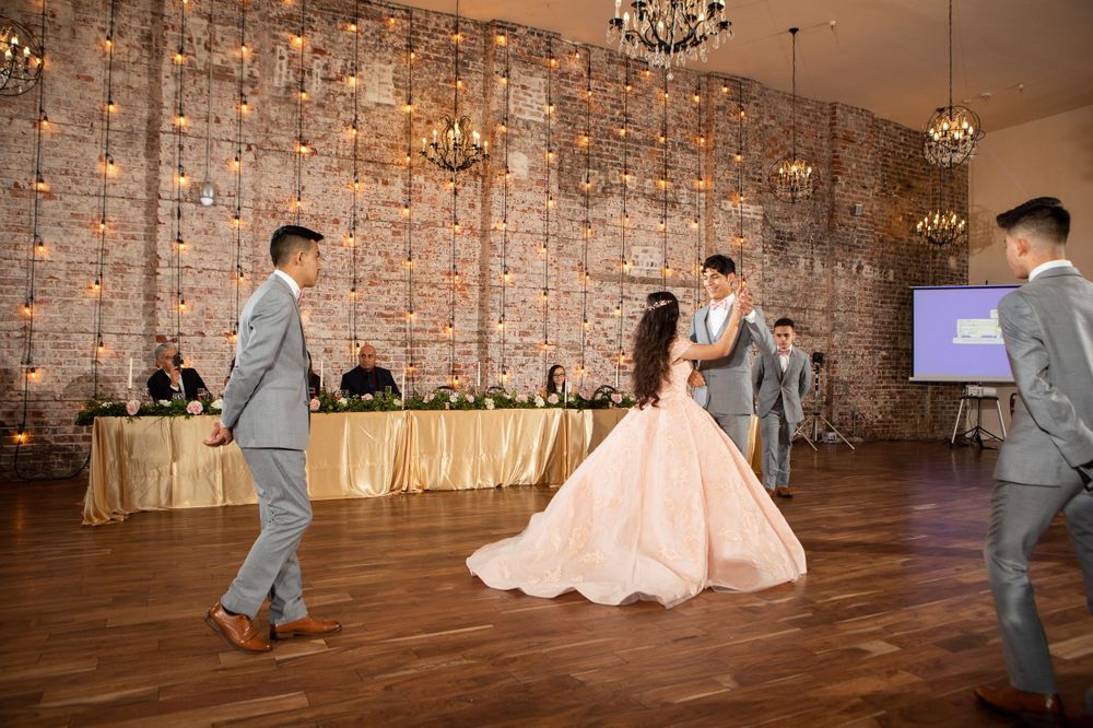 Dance performance in spacious ballroom with chandeliers and exposed brick walls.