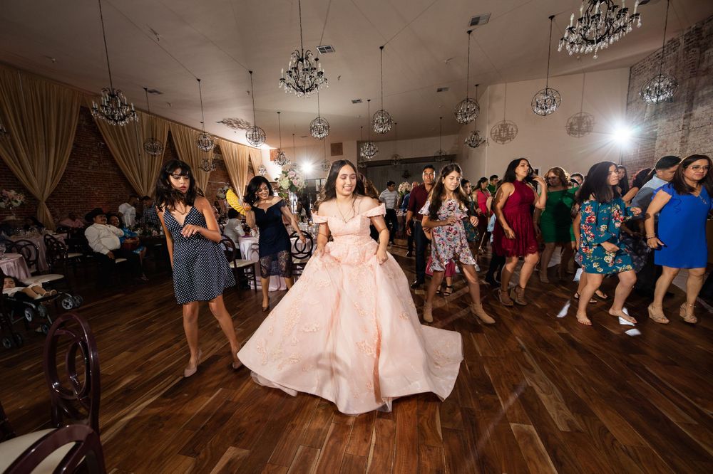 A celebration on a dance floor shows a person in a flowing pink ballgown surrounded by dancing party guests.