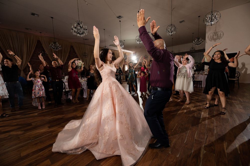 Partygoers dance enthusiastically with hands raised on a wooden floor under elegant lighting.