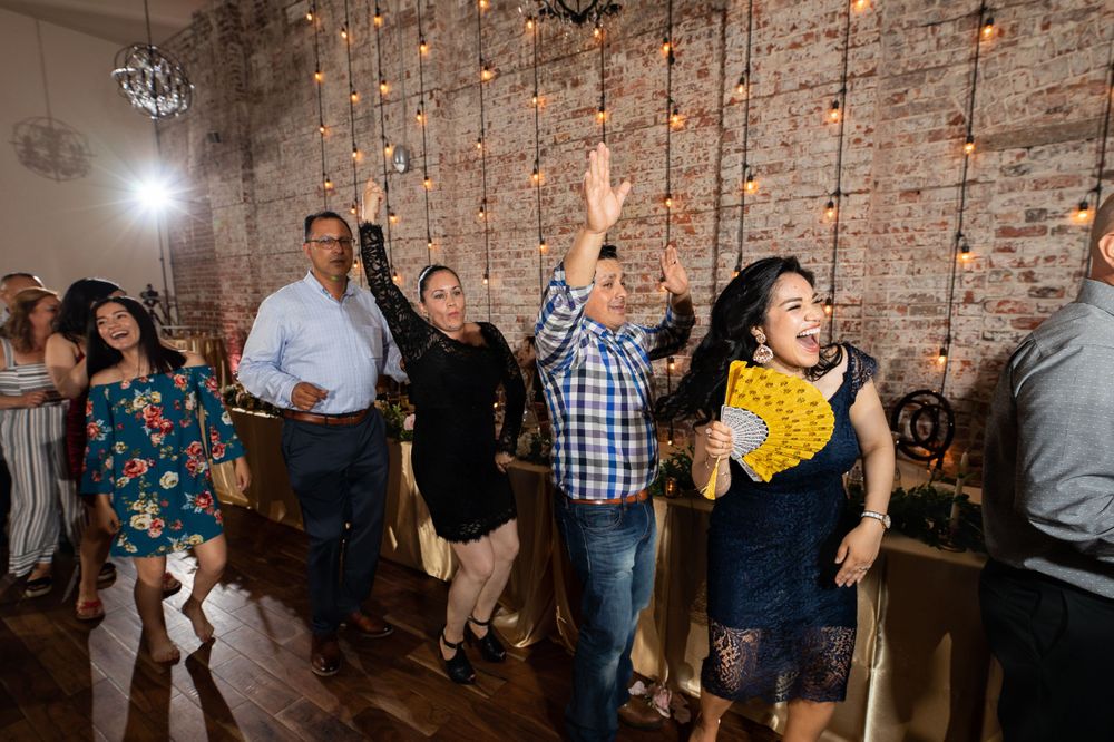 Party guests dance enthusiastically against an exposed brick wall with string lights.