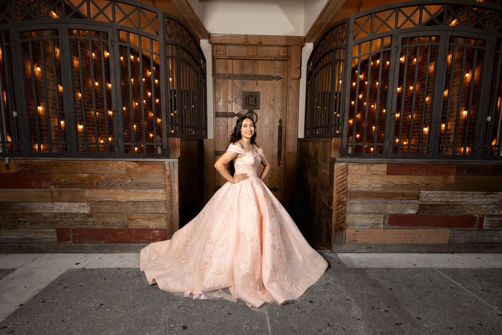 Stunning peach ballgown dress photographed in rustic venue with string lights.