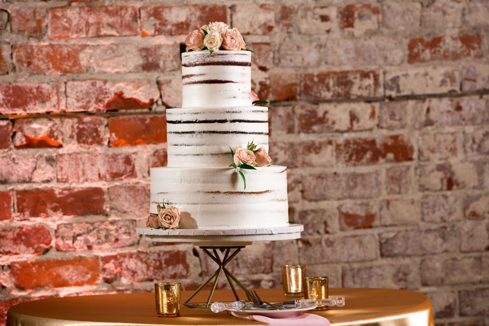 Elegant three-tier white wedding cake with floral accents against brick wall.