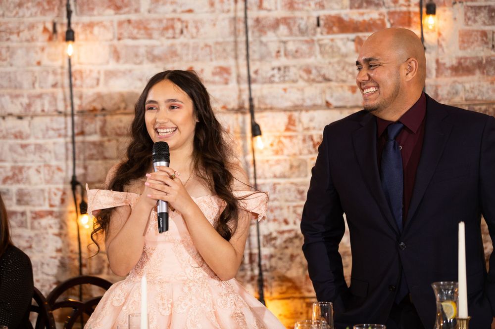 A formal celebration speech moment against an exposed brick wall with hanging lights.