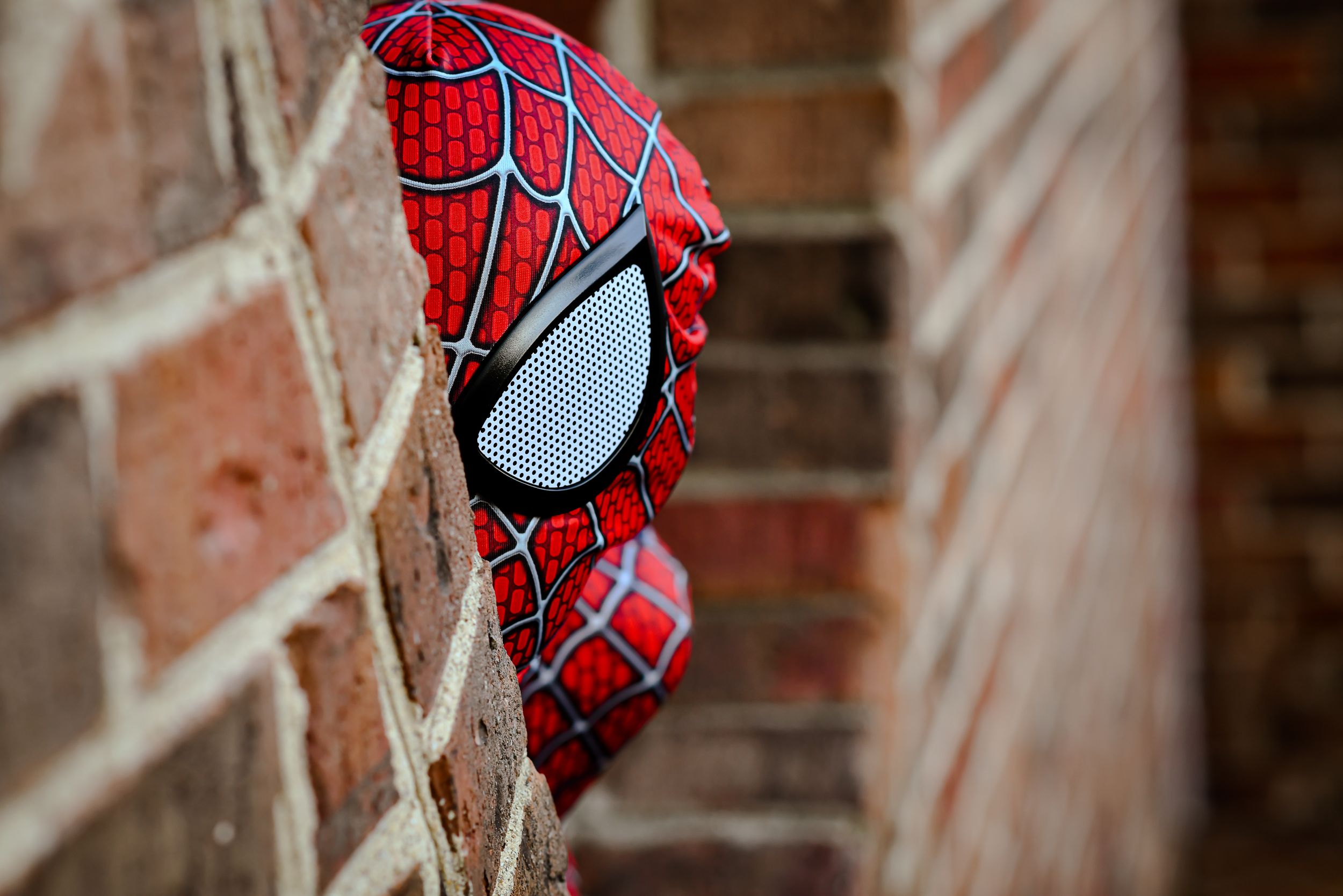 Close up detail of Spider-Man mask against a brick wall background.