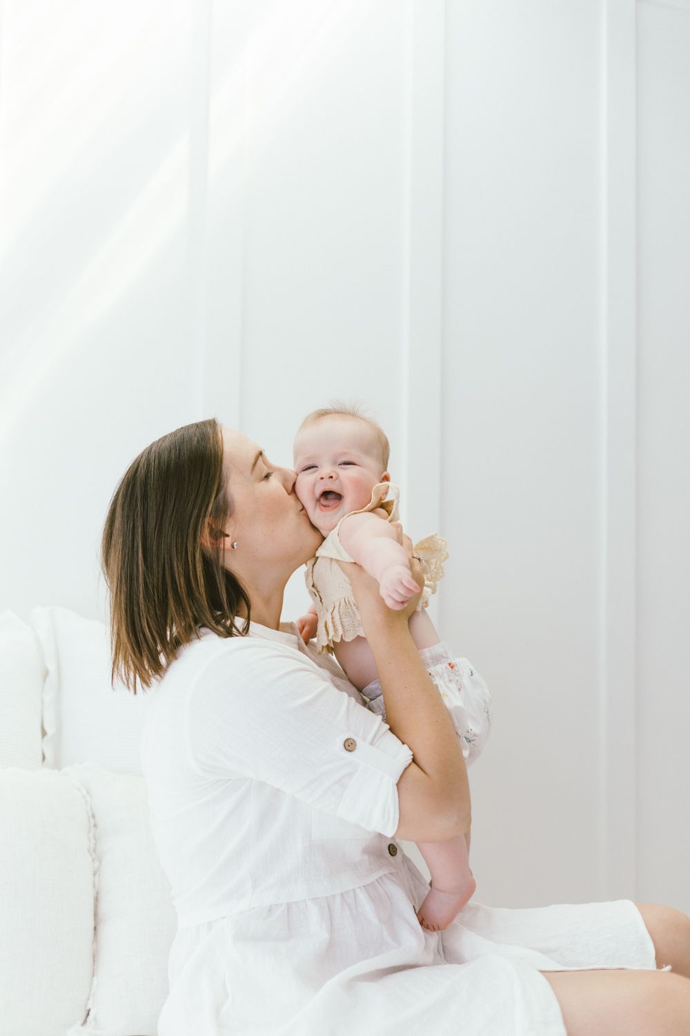 Loving playtime moment between parent and infant against bright white backdrop.