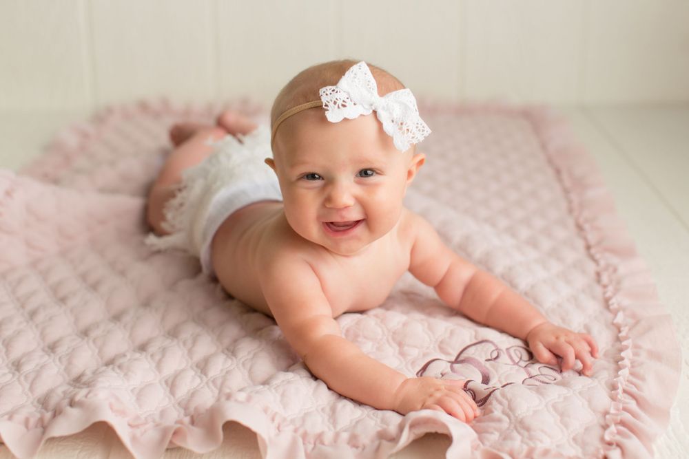 Joyful baby portrait on textured pink blanket with white bow accessory.
