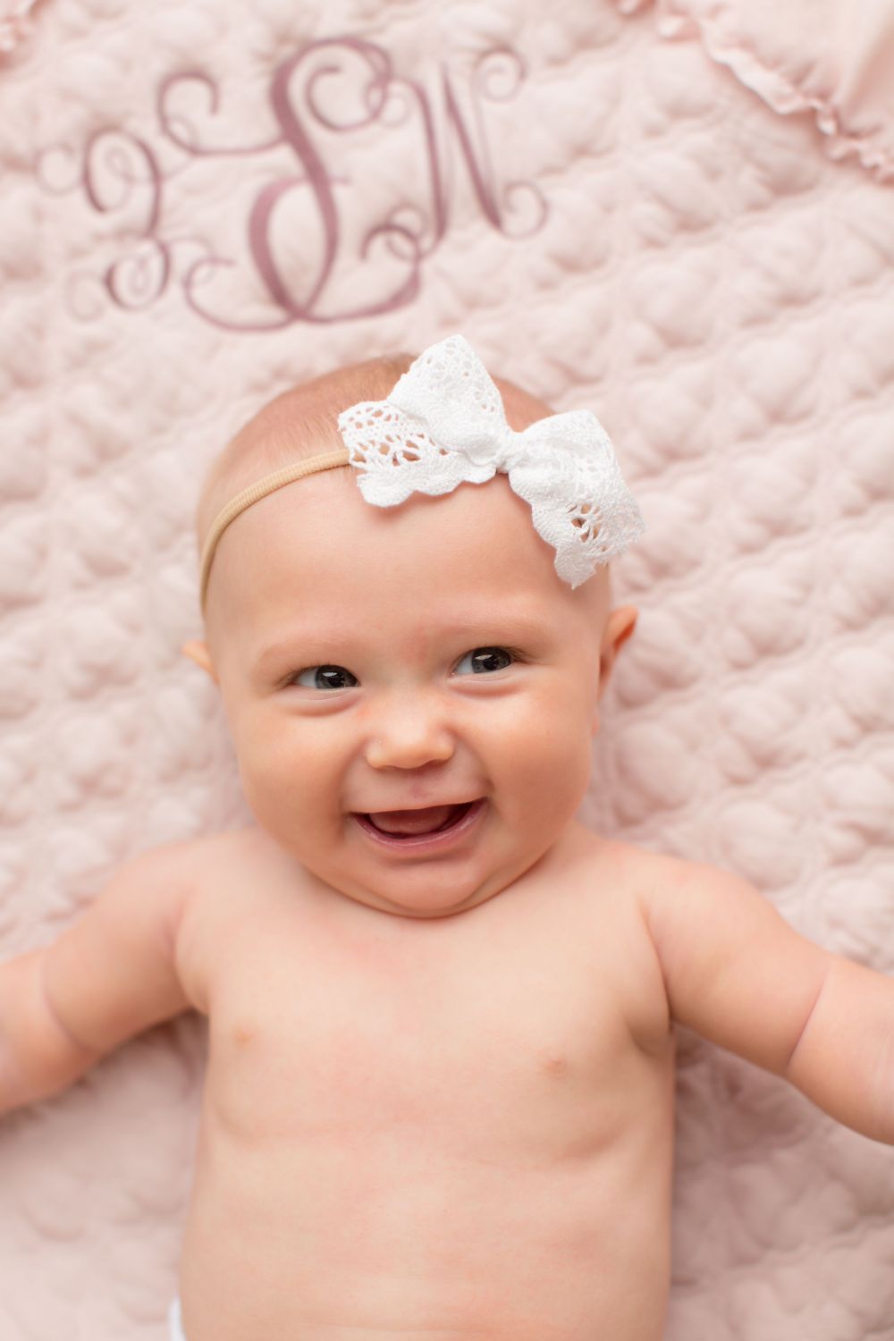 Baby portrait on monogrammed pink blanket wearing delicate white lace bow.