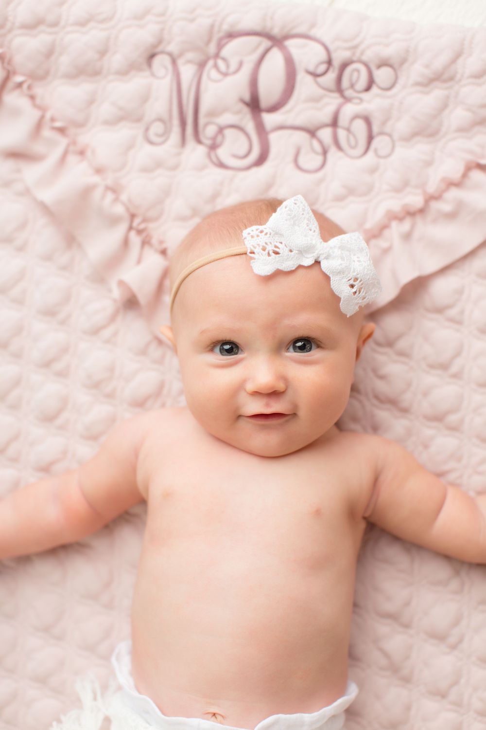 Sweet portrait against pink monogrammed blanket with white bow headband.