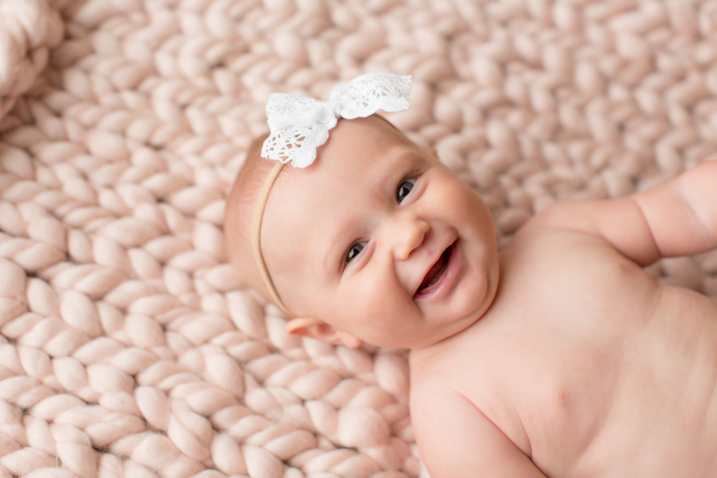 Laughing baby on pink knit blanket wearing white lace bow headband.