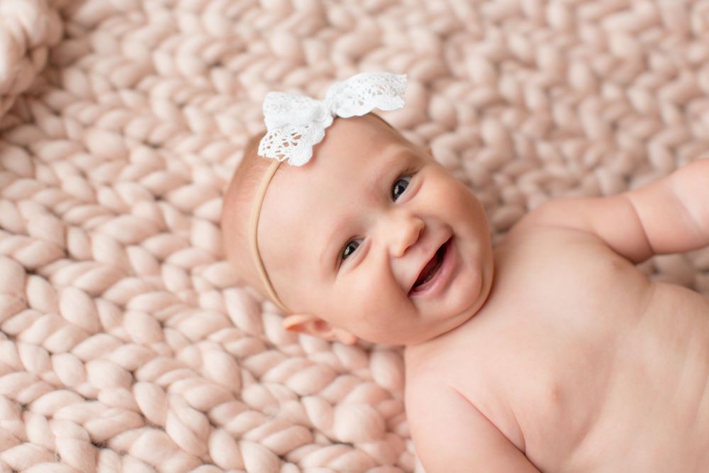 Laughing baby on pink knit blanket wearing white lace bow headband.